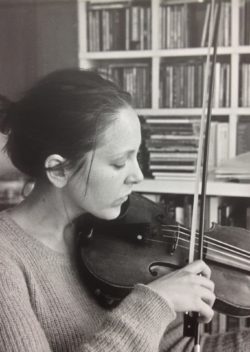 woman playing violin, bookshelf behind